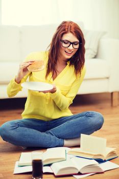 education and home concept - smiling student eating hamburger and doing homework at home