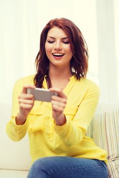 home, technology and internet concept - smiling woman playing with smartphone sitting on couch at home