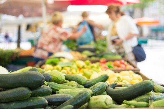 Farmers' food market stall with variety of organic vegetable. Vendor serving and chating with customers.