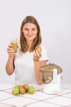 Young beautiful girl in the juicer squeezed pear juice and sitting at a table with a glass of juice in hand