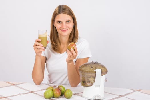 Young beautiful girl in the juicer squeezed pear juice and sitting at a table with a glass of juice in hand
