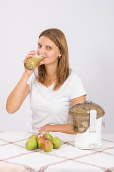 Young beautiful girl in the juicer squeezed pear juice and sitting at a table with a glass of juice in hand