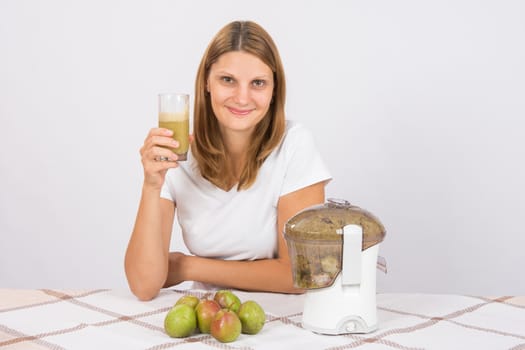 Young beautiful girl in the juicer squeezed pear juice and sitting at a table with a glass of juice in hand
