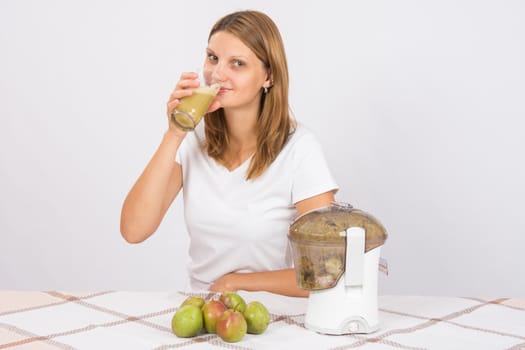 Young beautiful girl in the juicer squeezed pear juice and sitting at a table with a glass of juice in hand