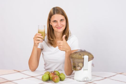 Young beautiful girl in the juicer squeezed pear juice and sitting at a table with a glass of juice in hand