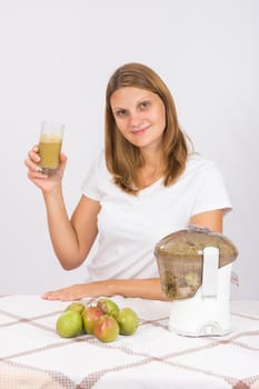 Young beautiful girl in the juicer squeezed pear juice and sitting at a table with a glass of juice in hand