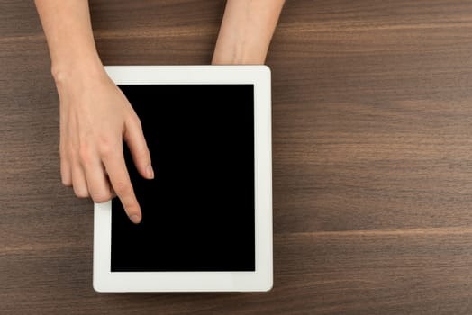 Womans hands pressing on tablet on wooden table background