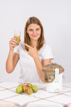 Young beautiful girl in the juicer squeezed pear juice and sitting at a table with a glass of juice in hand