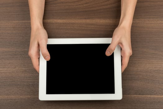 Humans hands holding tablet on wooden table background