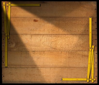 Frame made from a old wooden ruler on a weathered wooden background with planks and nails. Isolated on black background