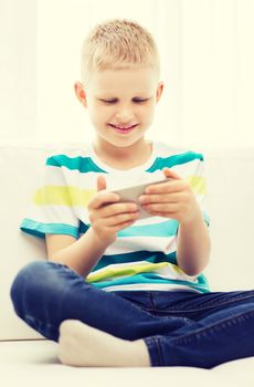 home, leisure, childhood, technology and game concept - little boy with smartphone at home