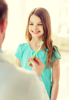 healthcare, child and medicine concept - male doctor giving toothbrush to smiling little girl