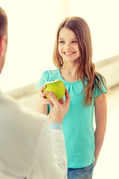 healthcare, child and medicine concept - male doctor giving an apple to smiling little girl