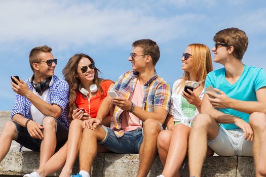 friendship, summer, technology and people concept - group of smiling friends with smartphones and headphones outdoors