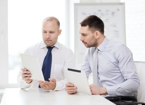 business, technology and office concept - two serious businessmen with tablet pc computers in office