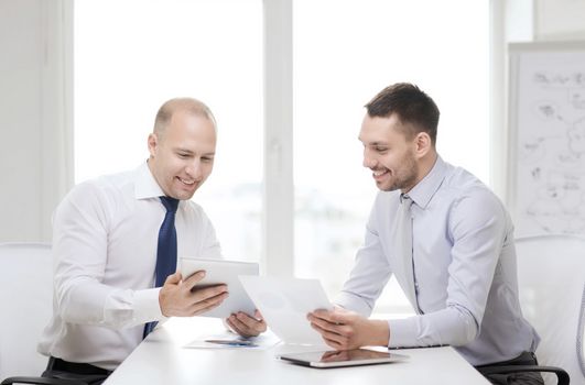 business, technology and office concept - two smiling businessmen with tablet pc computers and files in office