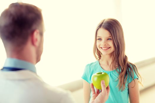 healthcare, child and medicine concept - male doctor giving an apple to smiling little girl