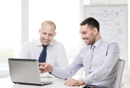 business, technology and office concept - two smiling businessmen with laptop in office