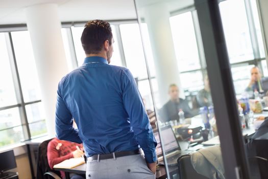 Business man making a presentation at office. Business executive delivering a presentation to his colleagues during meeting or in-house business training. View through glass.