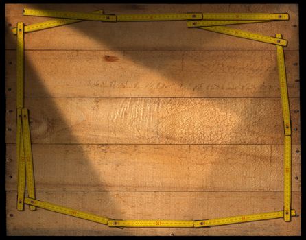 Frame made from a old wooden ruler on a weathered wooden background with planks and nails. Isolated on black background