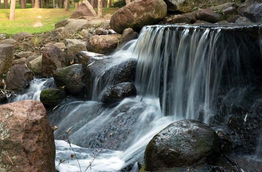 Poland.Park in Warsaw.Autumn.October.Small waterfall in the park.Ledge with the flow.Water falling from the top of the stones.Horizontal view.