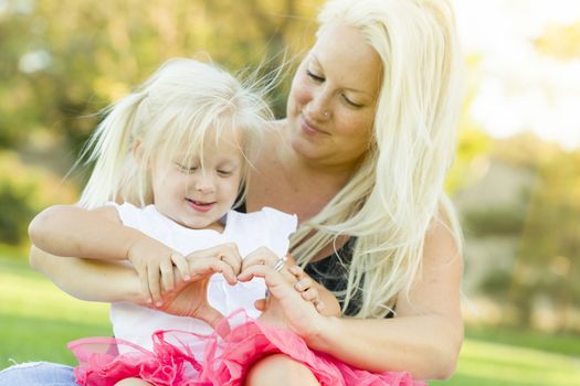 Cute Little Girl With Mother Making Heart Shape with Hands Outdoors.