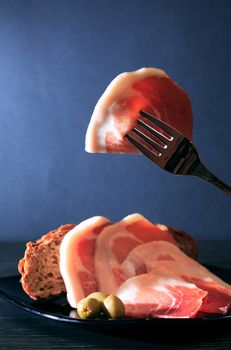 Italian prosciutto. Thin slice of prosciutto on fork above plate with meat