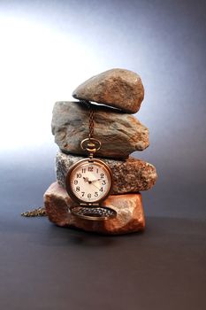 Pocket watch hanging on stones pyramid on dark background