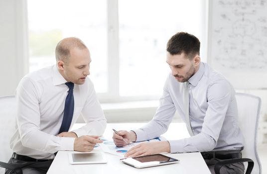 business, technology and office concept - two serious businessmen with tablet pc computers and files in office