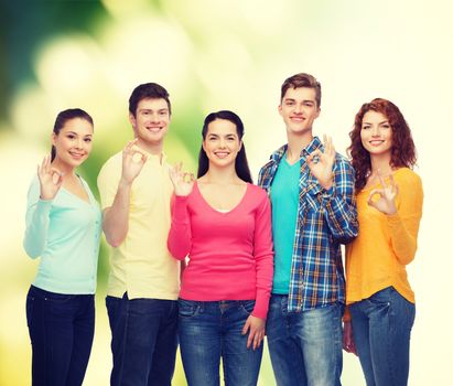 friendship, ecology, gesture and people concept - group of smiling teenagers showing ok sign over green background