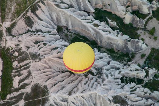 aerial shot of a yellow hot air balloon on top of cave volcanoes