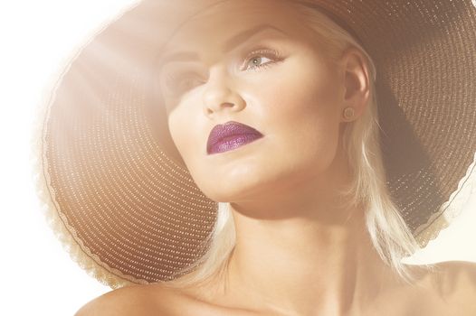 Close up head shot of a gorgeous sophisticated exotic young blond woman wearing a wide brimmed hat facing into sun flare