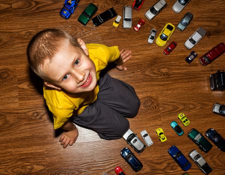 The photograph depicts a young boy with toy cars