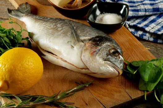 Cooking Raw Dorado Fish with Spinach, Anchovies, Herbs, Spices and Lemon closeup on Wooden Cutting Board