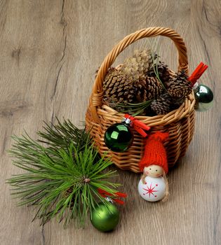 Christmas Decorations with of Fir Cones in Wicker Basket, Spruce Branches and Green Bauble with Handmade New Year Girl closeup Textured Wooden background