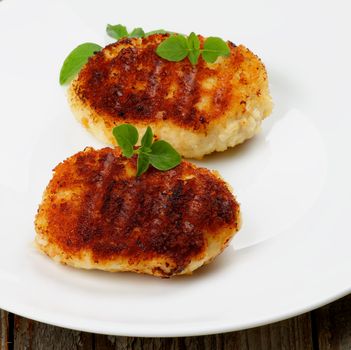Delicious Chicken Meat Cutlets Decorated with Basil on White Plate closeup on Wooden background