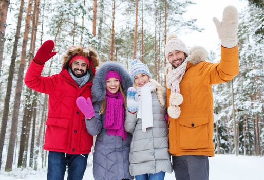 love, relationship, season, friendship and people concept - group of smiling men and women waving hands in winter forest