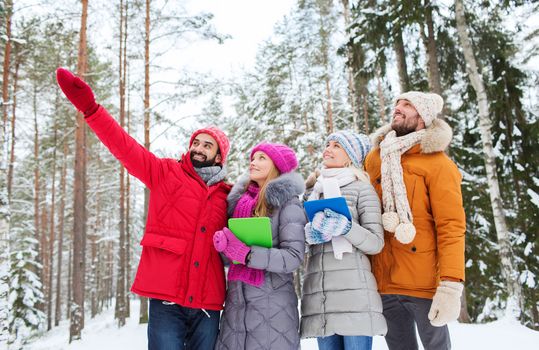 technology, season, friendship and people concept - group of smiling men and women with tablet pc computers pointing finger in winter forest