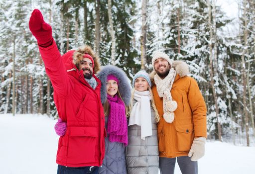 love, relationship, season, friendship and people concept - group of smiling men and women pointing finger in winter forest
