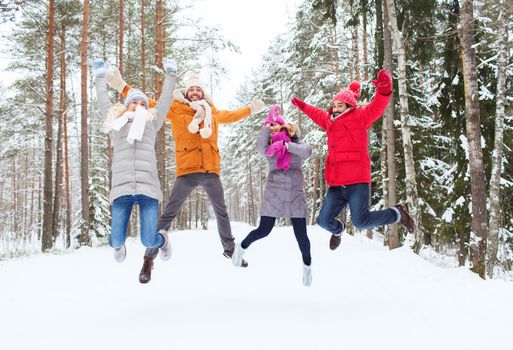 leisure, season, friendship and people concept - group of smiling men and women having fun and jumping in winter forest