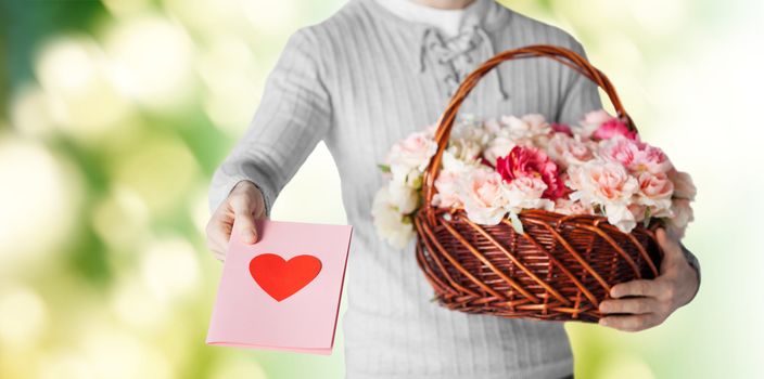 holidays, people, feelings and greetings concept - close up of man holding basket full of flowers and giving postcard over green background
