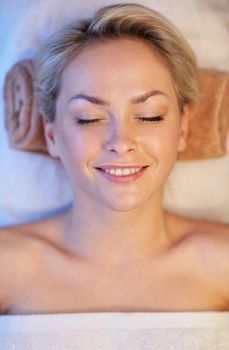 people, beauty, spa, healthy lifestyle and relaxation concept - close up of beautiful smiling young woman lying with closed eyes in spa