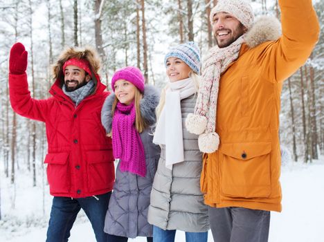 love, relationship, season, friendship and people concept - group of smiling men and women waving hands in winter forest