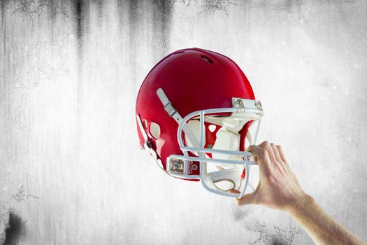 American football player holding up his helmet against grey background