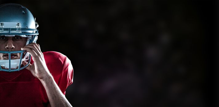 Portrait of American football player holding helmet against black background