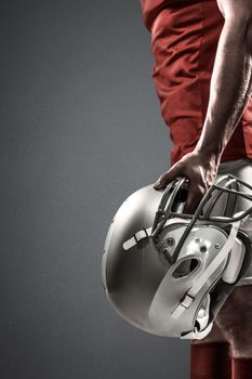 American football player holding helmet against grey