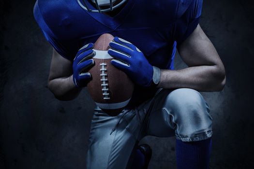 Mid section of American football player kneeling while holding ball against orange background