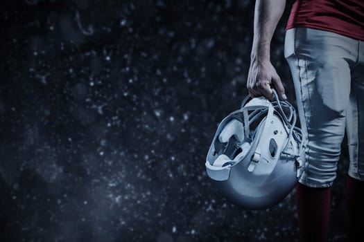 Cropped image of American football player holding helmet against black background