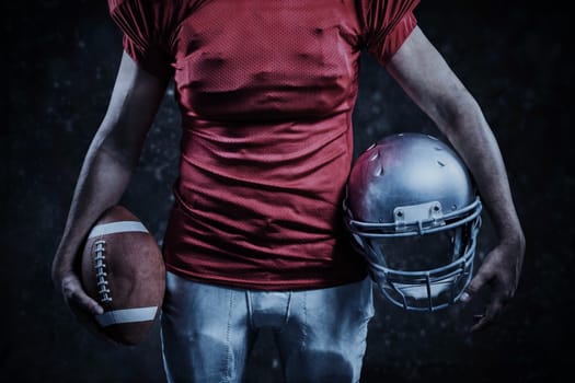 Mid section of sportsman holding American football and helmet against black background