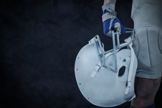 Close-up of American football player holding helmet against grey background